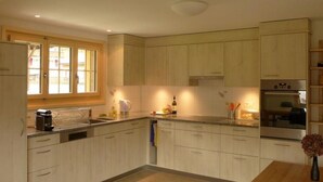 Een moderne keuken met lichte houten kastjes, een inbouwoven en een raam dat natuurlijk licht binnenlaat.