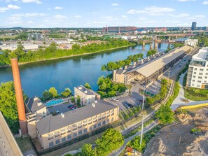 Ein Industriegebiet an einem Flussufer mit Gebäuden, einem großen Schornstein und einer Brücke im Hintergrund.