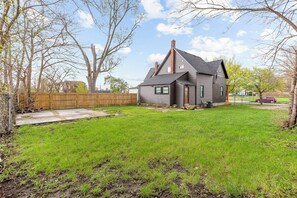 A residential house with a sloped roof, a chimney, and a fenced backyard.