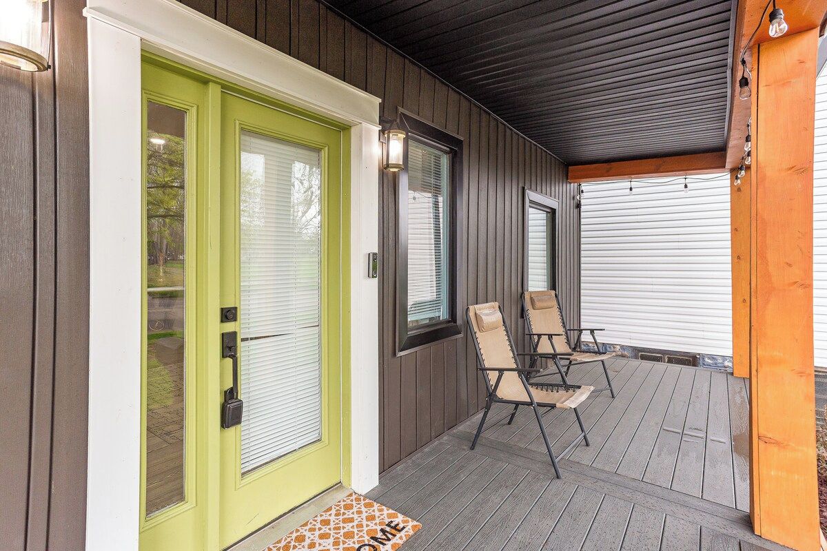 A covered porch with a green door, two chairs, and a doormat.