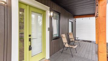 A covered porch with a green door, two chairs, and a doormat.