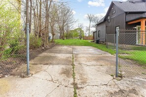 A concrete pathway leading to a residential property with a metal fence and a house with a dark exterior.