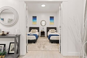 A bedroom with two beds, a bedside table, a mirror, and a view into another room. - Spacious 5BR in vibrant area, walk to cafes, restaurants & galleries (Detroit)