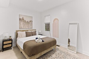 Une chambre à coucher avec un lit, des tables de chevet, un miroir et un tableau accroché au mur.