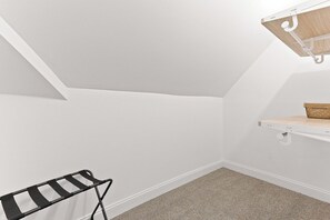A room with a sloped ceiling, a hanging rack, a shelf with a bag, and a carpeted floor.