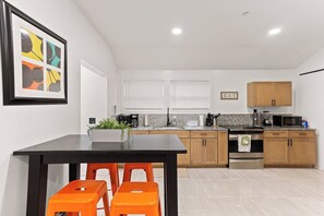 A modern kitchen with wooden cabinets, a black countertop, and a dining area with orange stools.
