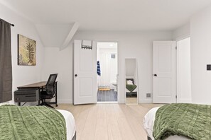 A bedroom with two beds, a desk, and a chair. There is a door leading to a bathroom.