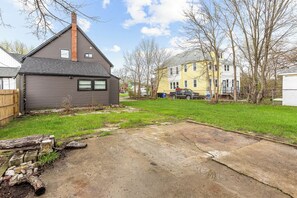A residential backyard with a paved area, a wooden fence, and a house with a chimney.