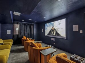 Una habitación de tonos oscuros con una pantalla grande, asientos amarillos y anaranjados y un proyector.