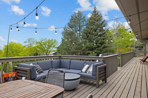 A deck with a sectional sofa, a round table, and string lights.
