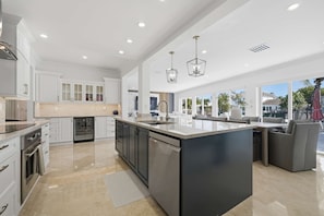 A spacious kitchen with a large island, white cabinetry, and a dining area with a sofa. - Coral Hall – Where the intracoastal meets luxury (Fort Lauderdale)