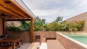 Eine Terrasse im Freien mit Holzmöbeln, einem Pool und üppiger Bepflanzung.