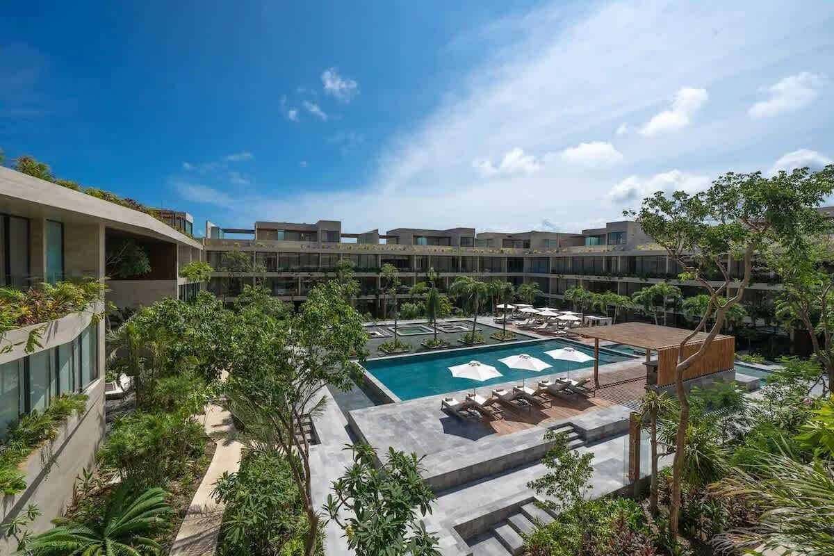 A hotel with a swimming pool, lounge chairs, and a covered area.