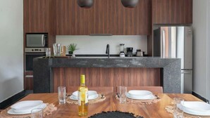 A modern kitchen with wooden cabinets, a granite countertop, and a dining area with a wooden table set for two. - Luxury Jungle Villa with Private Pool & Concierge (Tulum)