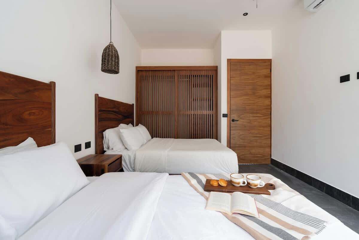 A hotel room with two beds, a wooden wardrobe, a hanging light fixture, and a breakfast tray on the bed.