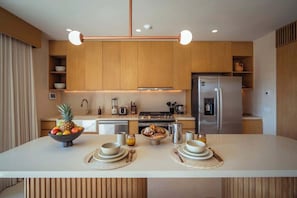 Eine moderne Küche mit Holzschränken, einer zentralen Kochinsel mit Frühstücksangeboten, einem Kühlschrank und einem Herd.
