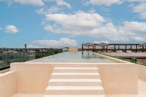 Ein Rooftop-Endlospool mit Treppen, die zum Pool hinabführen, umgeben von Liegestühlen und Sonnenschirmen.
