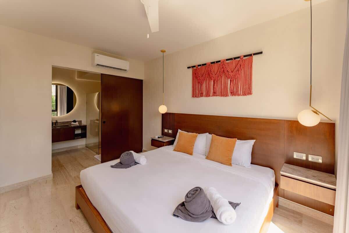 Une chambre d’hôtel avec un grand lit, une tête de lit en bois, un climatiseur fixé au mur et une petite table de chevet avec une lampe.