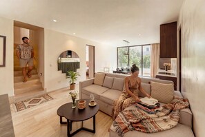A modern living room with a sofa, a coffee table, and a dining area with a kitchen in the background. - Sleek Penthouse Escape with Rooftop Pool (Tulum)
