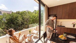 Eine moderne Küche mit dunklen Holzschränken, ein Essbereich mit Tisch für zwei Personen und ein Balkon mit Blick auf Bäume.
