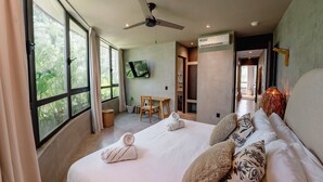 Een moderne hotelkamer met een groot bed, een plafondventilator, een flatscreen televisie en uitzicht op groen door de ramen.
