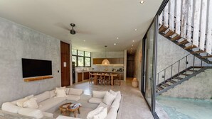 Een ruime woonkamer met een grote hoekbank, een flatscreen televisie en een keuken op de achtergrond.