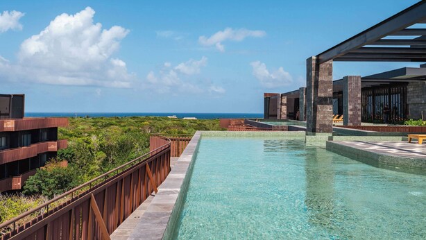 A pool with a clear view of the ocean, surrounded by modern buildings with balconies. - AMIRA Luxury 3BR PH with Rooftop and private pool (Tulum)