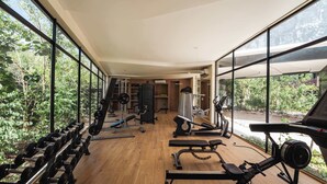 A gym with exercise equipment, large windows, and a view of greenery. - AMIRA Luxury 3BR PH with Rooftop and private pool (Tulum)