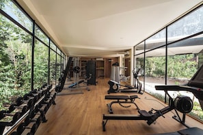 Ein Fitnessraum mit Trainingsgeräten, großen Fenstern und Blick auf Grünflächen.