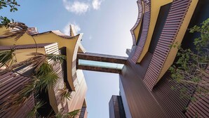 A modern building with a unique architectural design, featuring a central glass bridge and surrounding structures with sloped roofs. - AMIRA Luxury 3BR PH with Rooftop and private pool (Tulum)