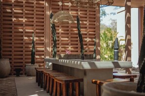 A bar area with a counter, stools, and a decorative cactus plant. - Chic Aldea Zama Condo with Pool & Parking (Tulum)
