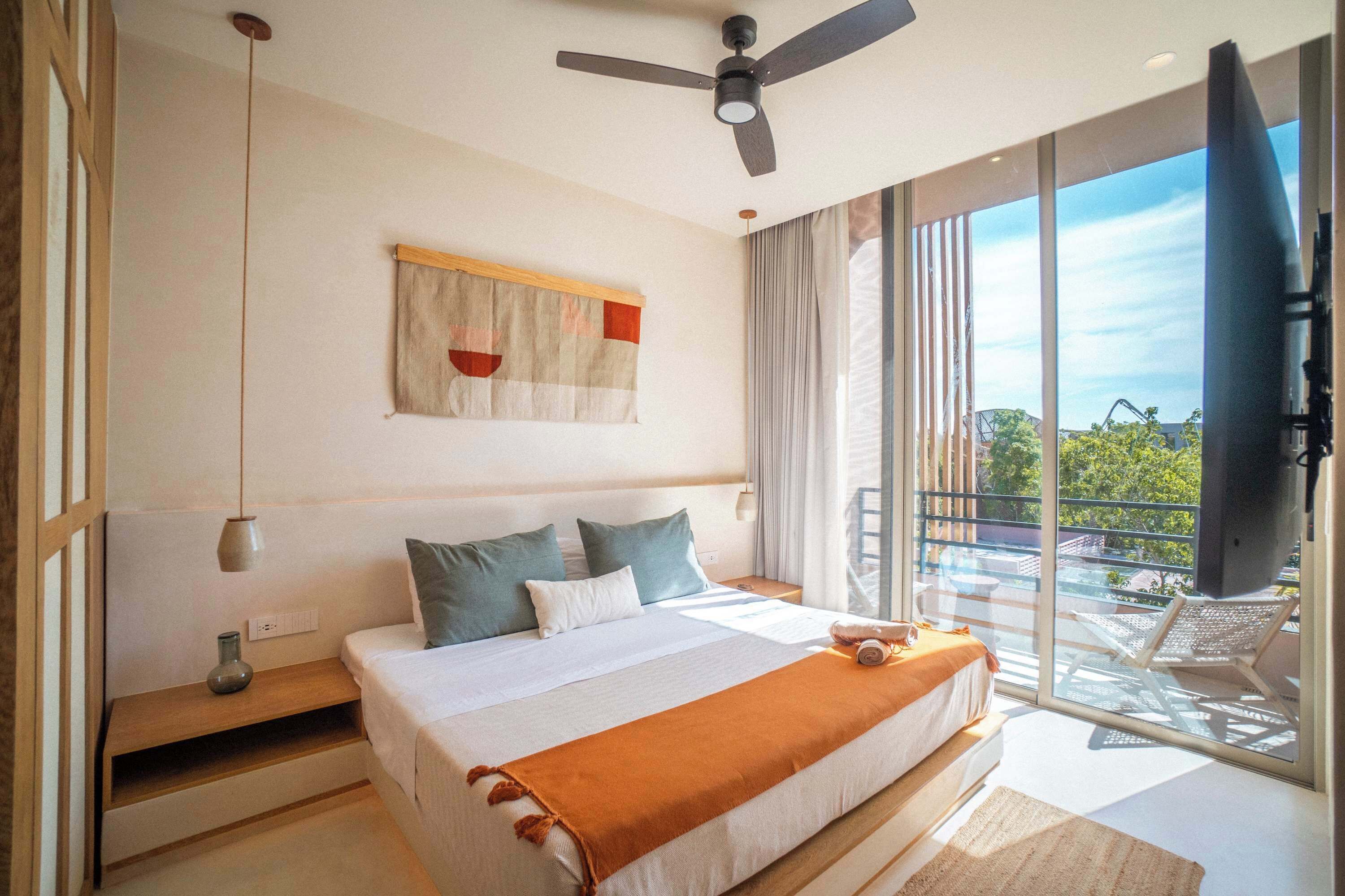 Une chambre à coucher avec un lit, un ventilateur de plafond, une fenêtre avec des rideaux et une vue sur l’extérieur.