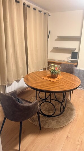 Une table de salle à manger ronde en bois, agrémentée d’un centre de table en forme de panier tressé, une seule chaise marron et un tapis moelleux.