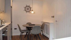 Cozinha compacta com área de refeições, decoração de roda de navio e uma porta branca.