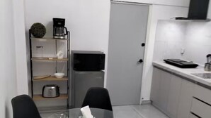 Una cocina compacta con una mesa de vidrio, dos sillas, cafetera, microondas y refrigerador pequeño.