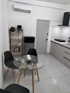 Eine kleine Küche mit einem Glastisch, zwei Stühlen, einer Kaffeemaschine, einer Mikrowelle und einem kleinen Kühlschrank.