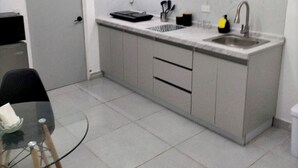 Cocina compacta con lavamanos, encimera y una mesa de vidrio con sillas.