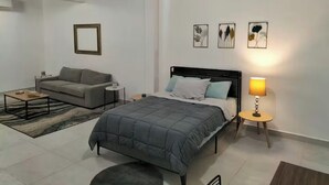 Un dormitorio moderno con una cama, un sofá, una mesita y una lámpara.