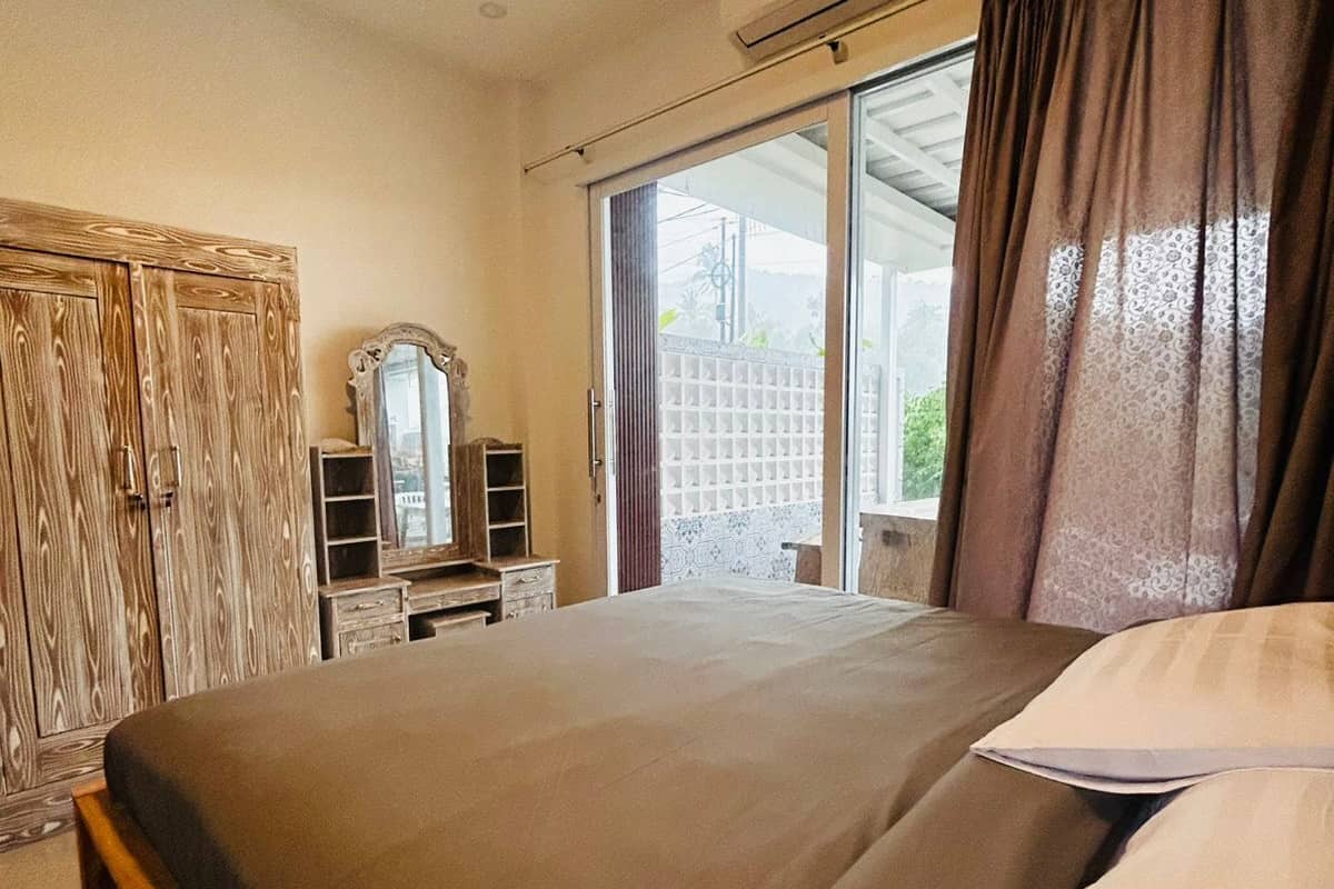 Une chambre à coucher comprenant un lit, une commode, un miroir et une porte-fenêtre coulissante donnant sur l’extérieur.
