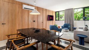 Ein modernes Wohnzimmer mit einer Wandpaneelaus Holz, einem schwarzen Marmortisch, blauen Sesseln, einem grauen Sofa und einem an der Wand montierten Fernseher.