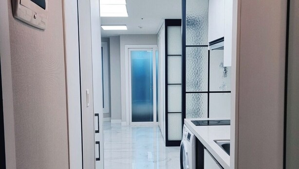 Un couloir d’hôtel moderne, équipé d’un lave-linge, d’un porte-chaussures et d’une porte donnant sur une autre pièce.