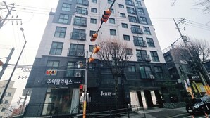Un immeuble à plusieurs étages, doté d’une entrée noire et d’une enseigne portant le nom « Jenny », et entouré d’infrastructures urbaines.
