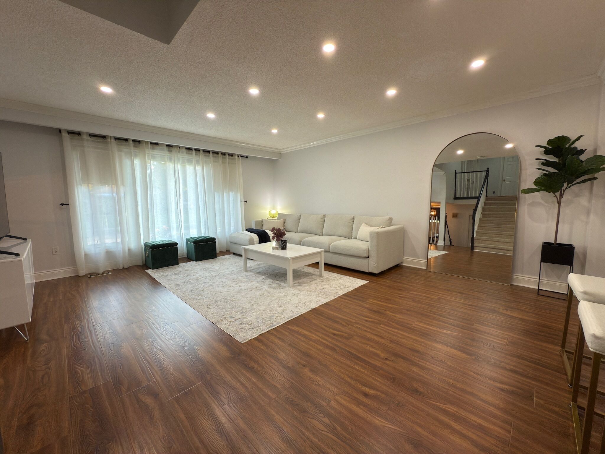 Amplia sala de estar con un sofá blanco, una mesa de centro y un espejo grande que refleja la escalera.
