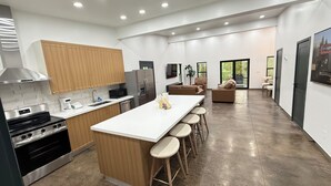 A modern kitchen with a central island, bar stools, a dining area with a sofa, and a view of the outdoors.