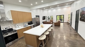A modern kitchen with a central island, bar stools, a dining area with a sofa, and a view of the outdoors.