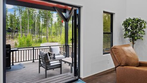 A room with a sliding glass door leading to a deck, a brown leather chair, a small table, and a potted plant.