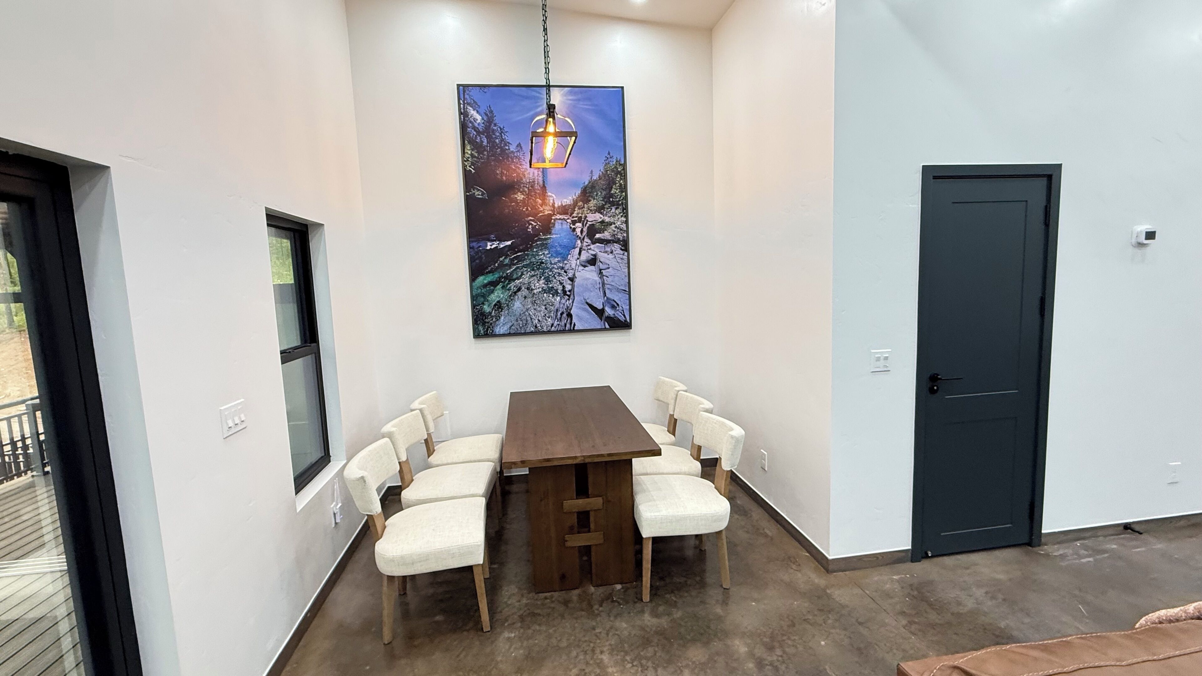 A dining area with a table and chairs, a painting of a landscape, a door, and a window.