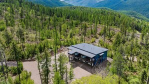 A cabin with a metal roof, surrounded by dense forest and mountains in the background.