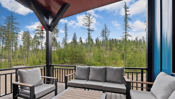 A deck with a sofa, chairs, and a table, overlooking a forest.