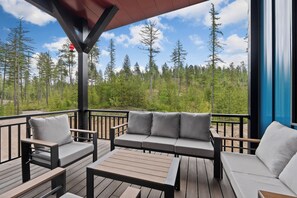 Eine Terrasse mit einer Couch, Stühlen und einem Tisch, mit Blick auf einen Wald.